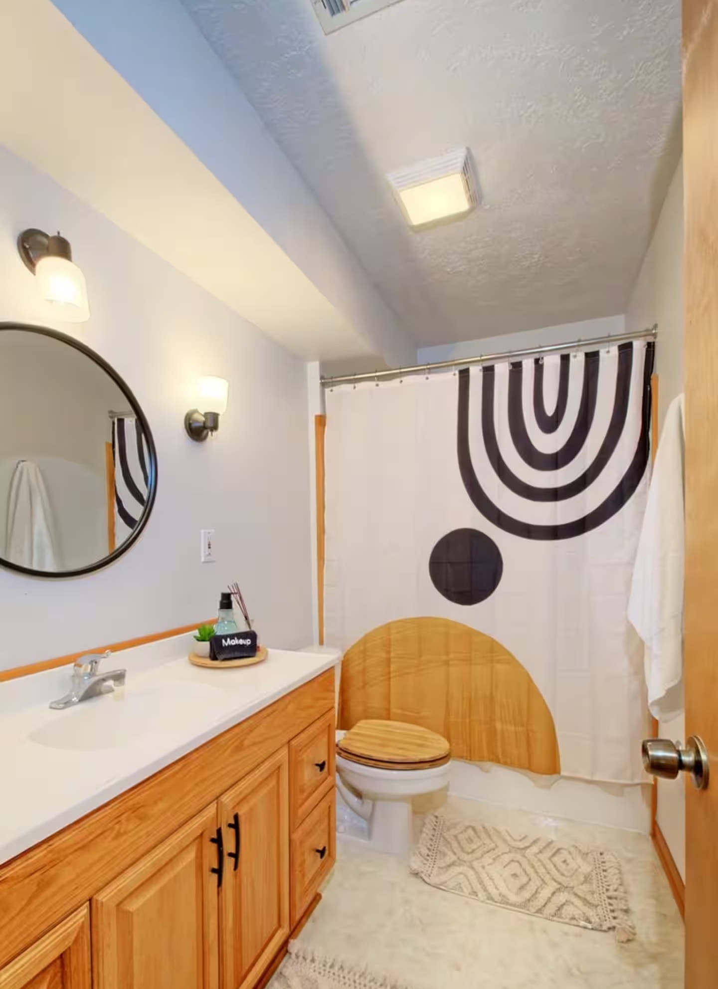 Downstairs bathroom with wood vanity, round mirror, and geometric shower curtain