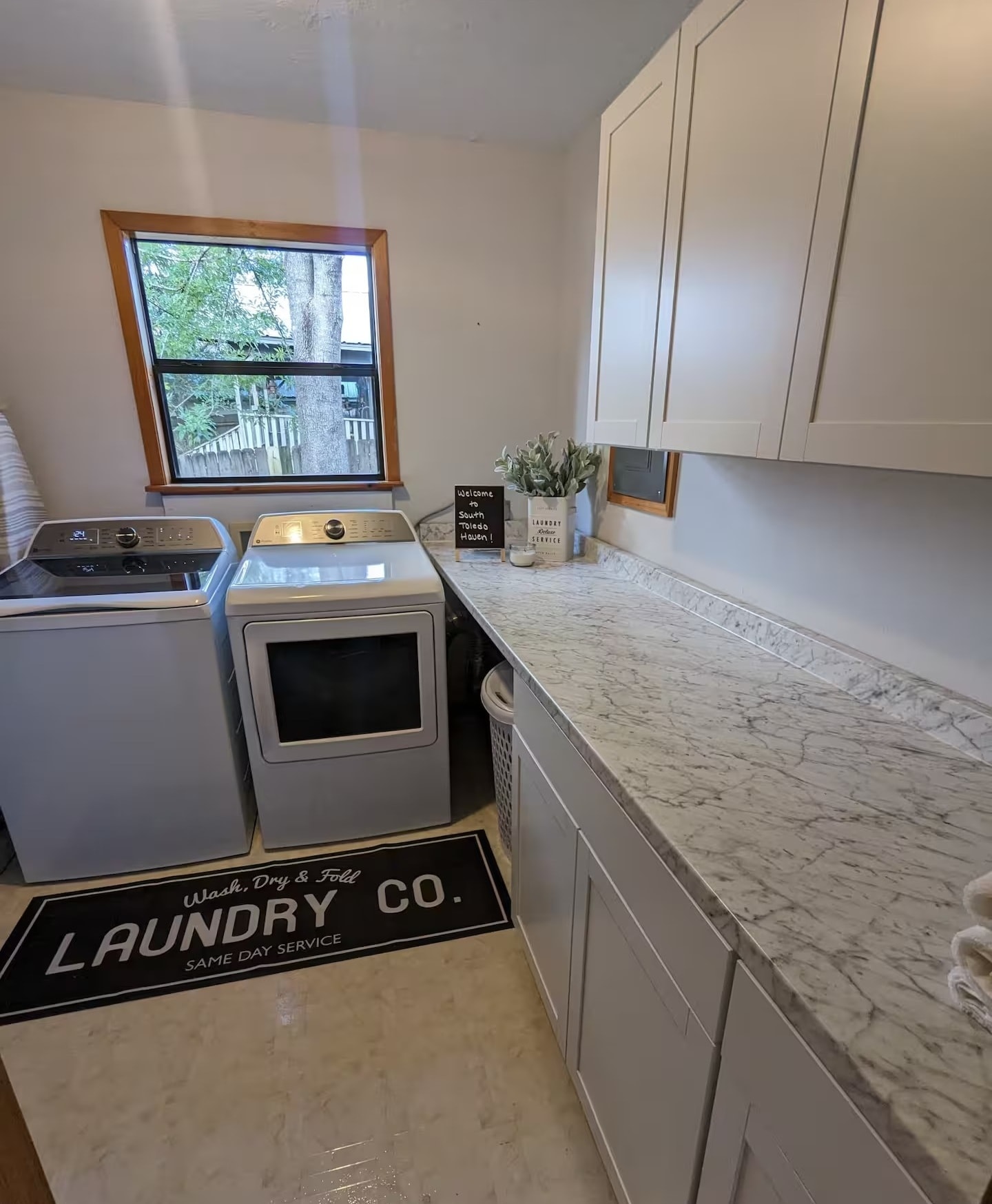 Laundry room with full-size washer and dryer, marble countertops, and white cabinetry